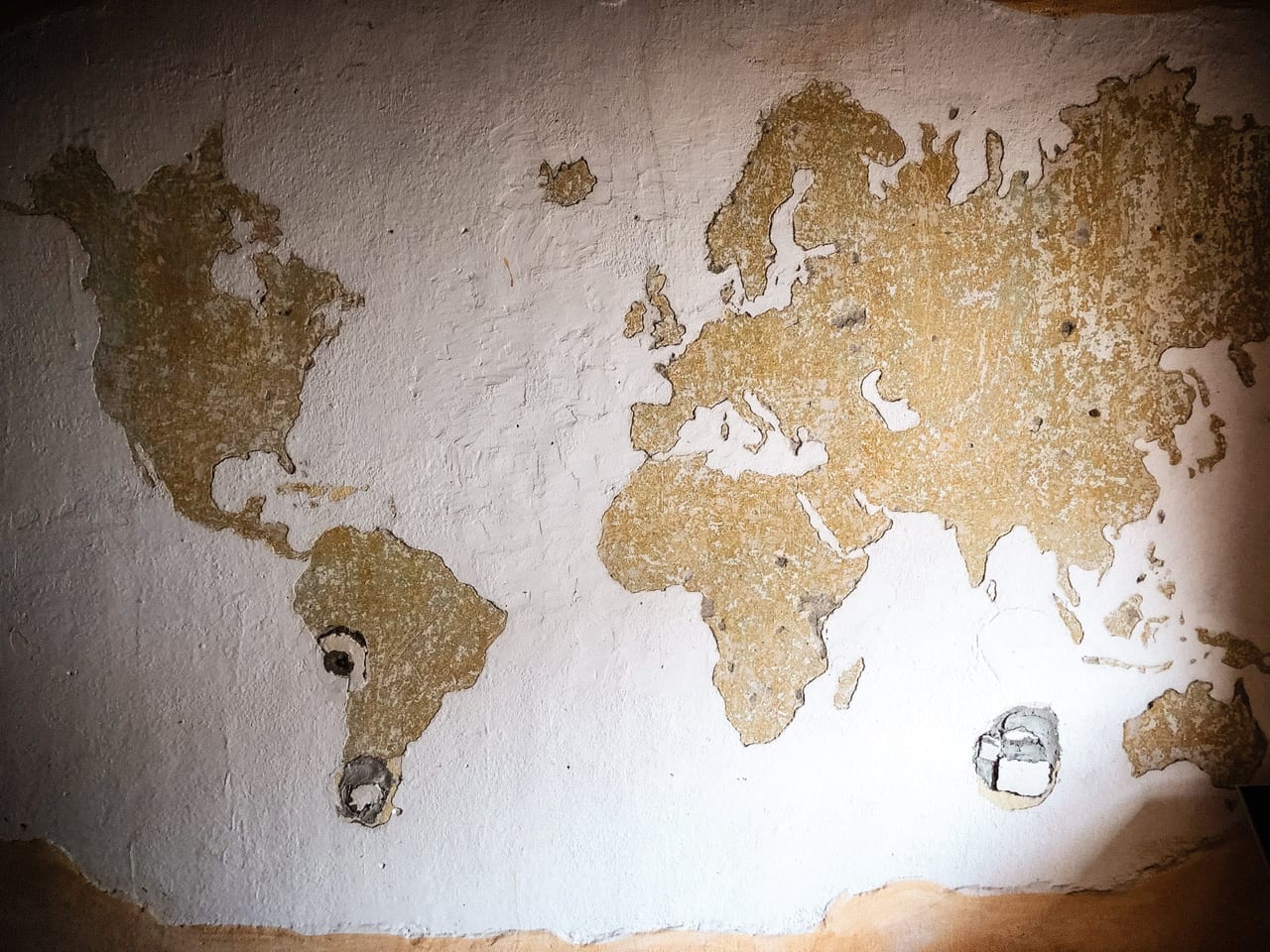 A world map, painted and worn into a white wall