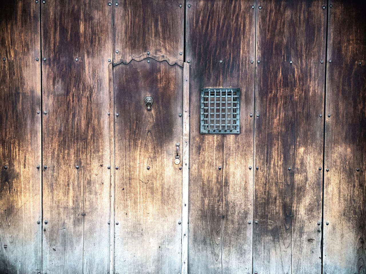 A grey wooden door with a small iron grille