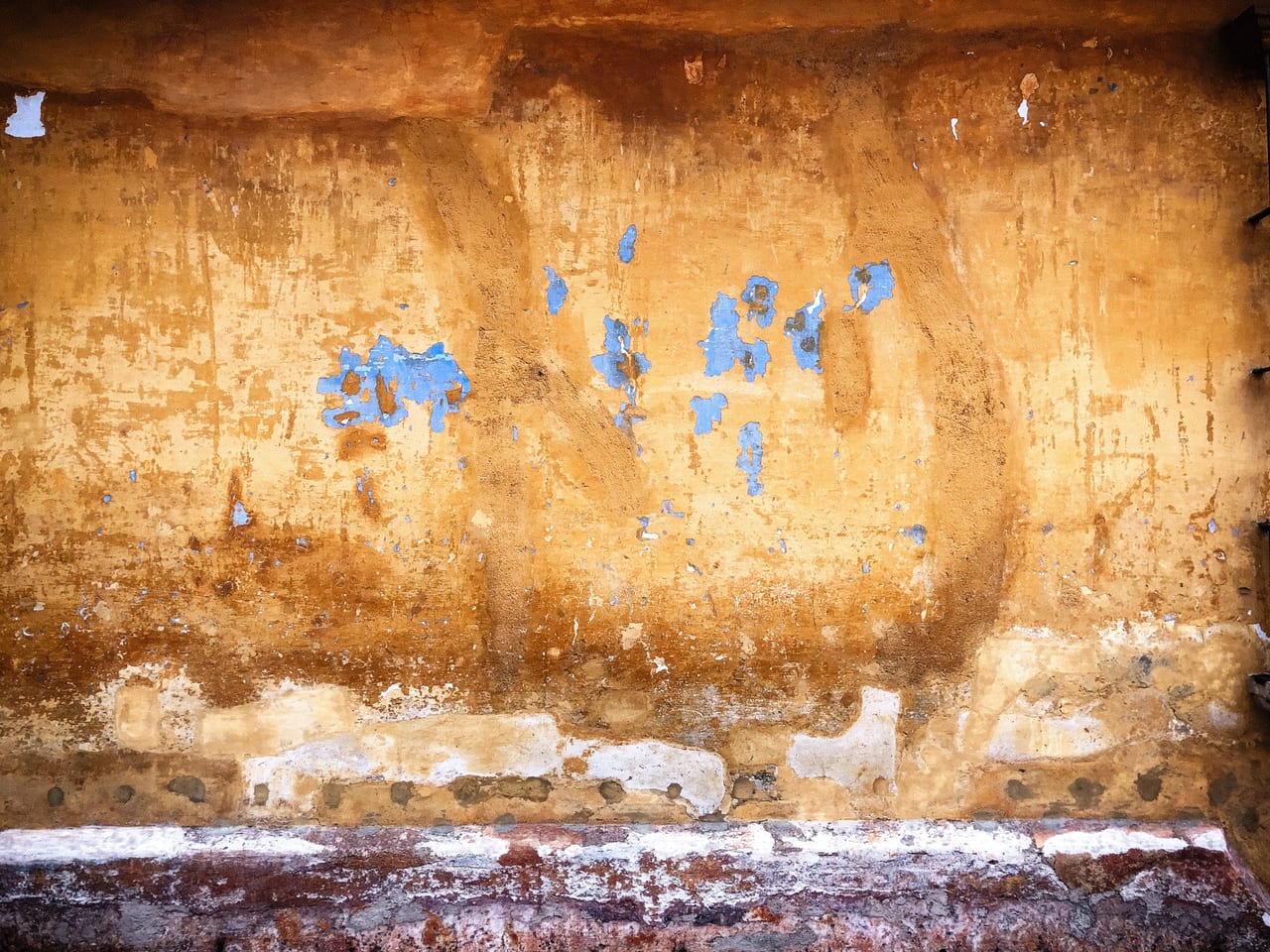 A peeling ochre wall with a grey plinth
