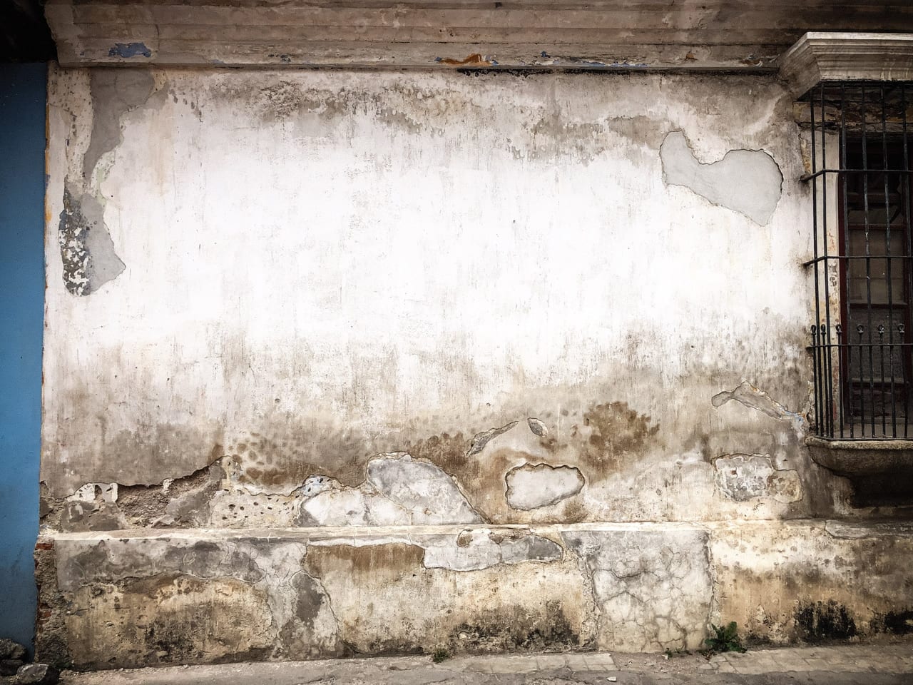 A cracked cream wall beside a barred window